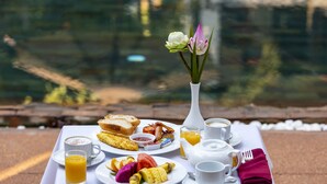 Una mesa de desayuno con platos de comida, un jarrón de flores y vistas a un cuerpo de agua.