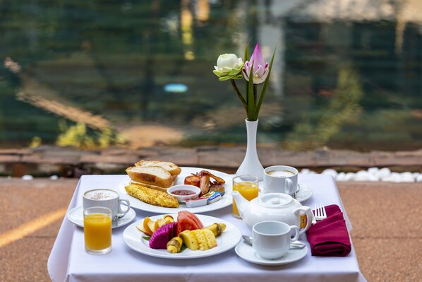 Una mesa de desayuno con platos de comida, un jarrón de flores y vistas a un cuerpo de agua.