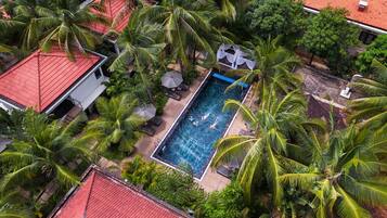 Relax by the tranquil pool surrounded by lush greenery and palm trees.