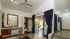 Amplia sala de estar con ventilador de techo, un espejo grande, una mesa de centro con un florero y vista a una piscina a través de una puerta de cristal.
