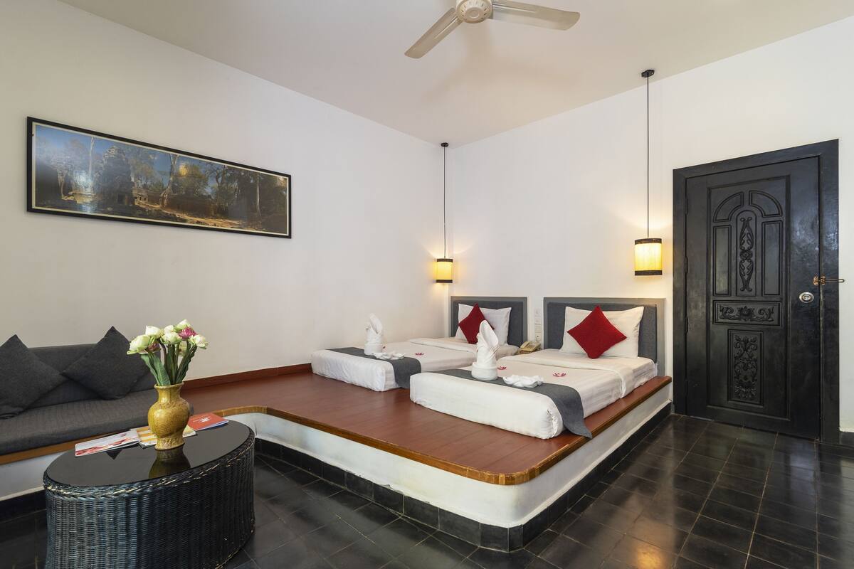 A hotel room with two beds, a sofa, a coffee table, a painting, and a door.