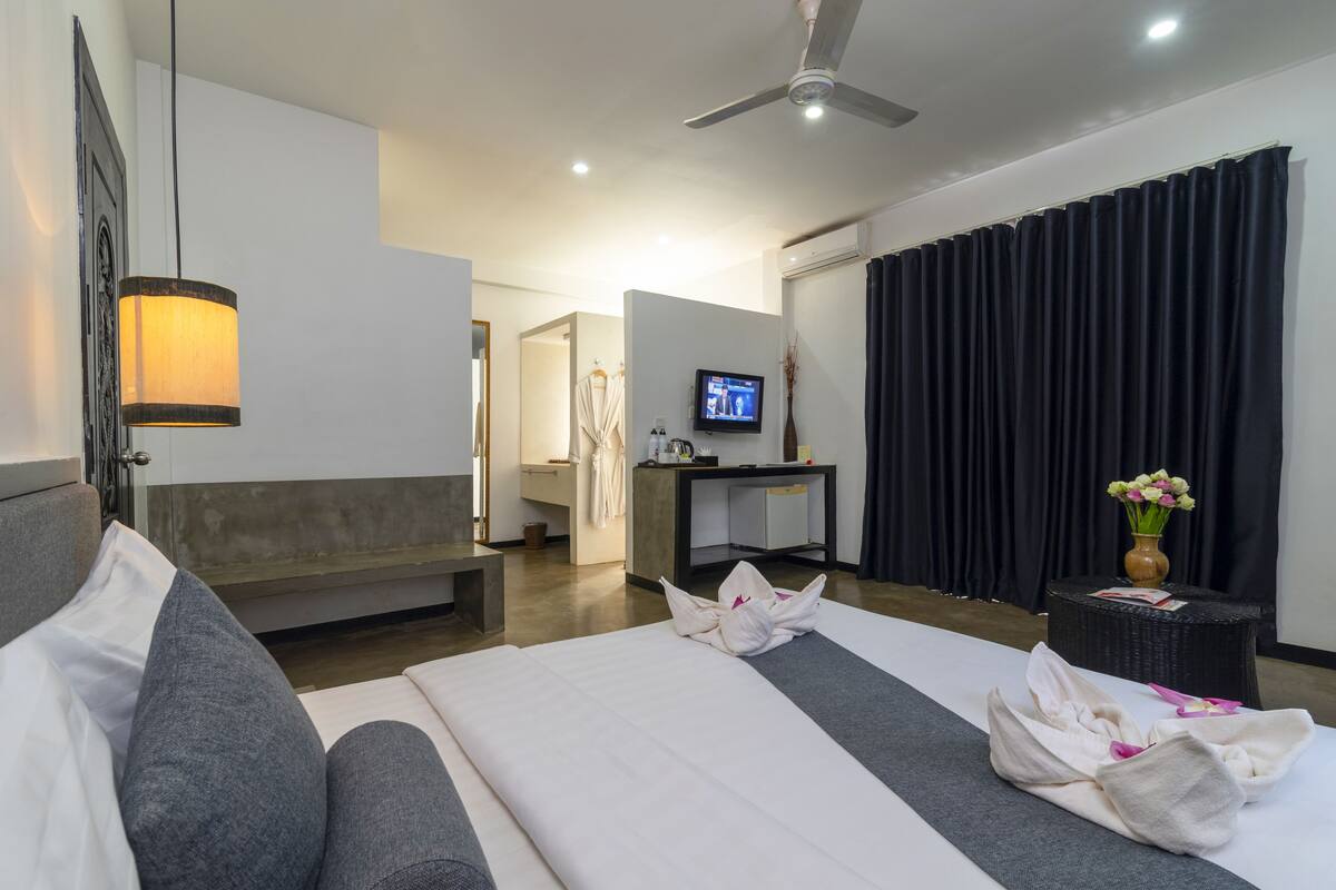 A hotel room with a bed, a sofa, a desk, a television, and a ceiling fan.
