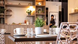 Une cuisine moderne avec des meubles en bois, une table à manger dressée avec de la vaisselle en verre transparent et une plante en pot posée sur le comptoir.