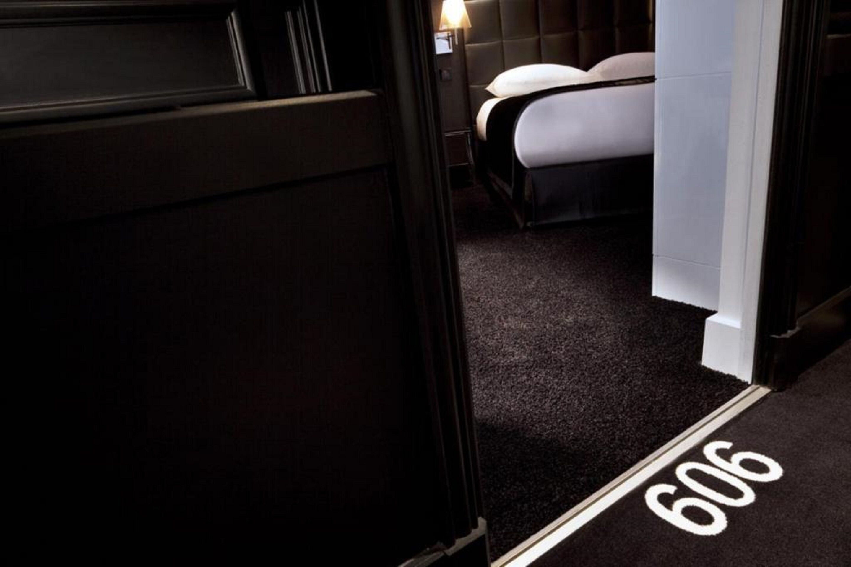 A hotel room with a dark carpet, a bed with white bedding, and a visible room number 606.