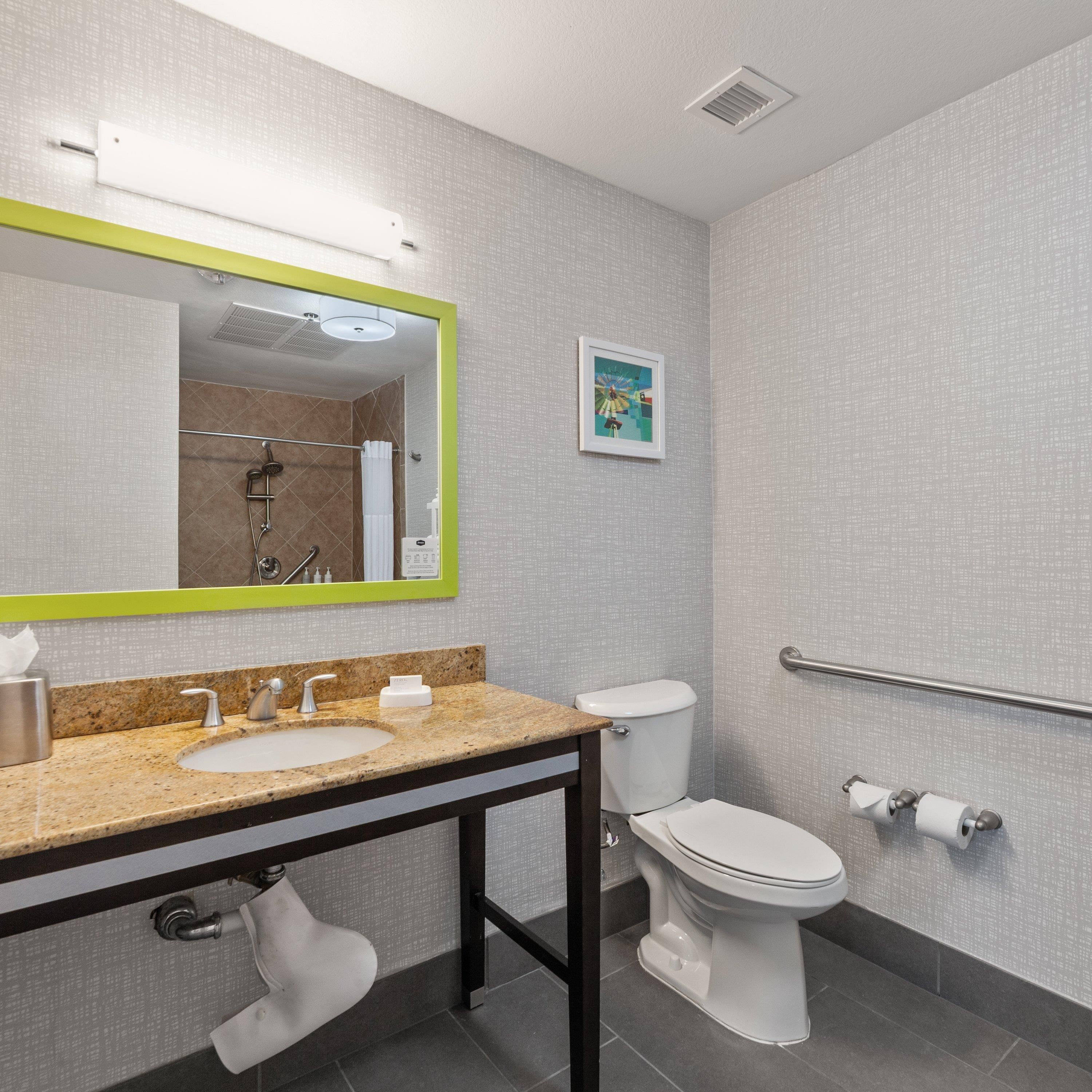 A modern bathroom with a granite countertop sink, a white toilet, and a shower area.