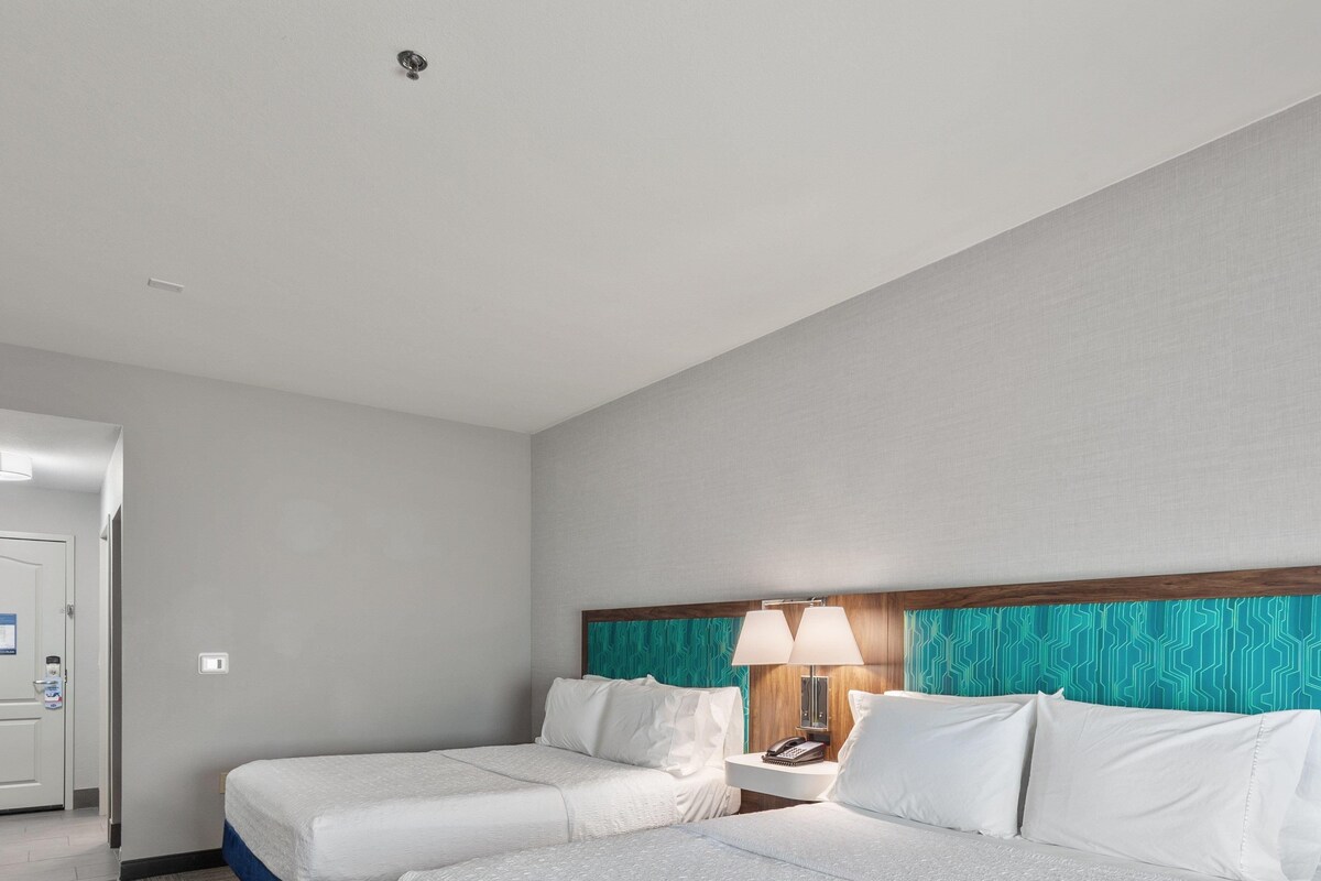 A hotel room with two beds, a nightstand with a lamp, and a door with a lock.