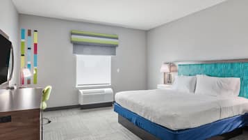 Una habitación de hotel con cama, mesita de noche, lámpara y escritorio con silla.