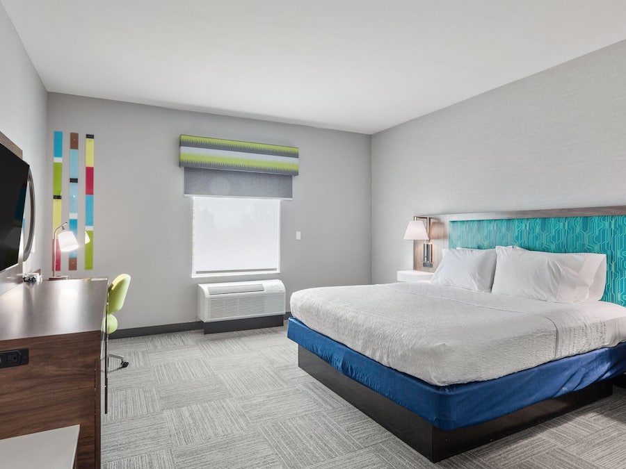 Una habitación de hotel con cama, mesita de noche, lámpara y escritorio con silla.
