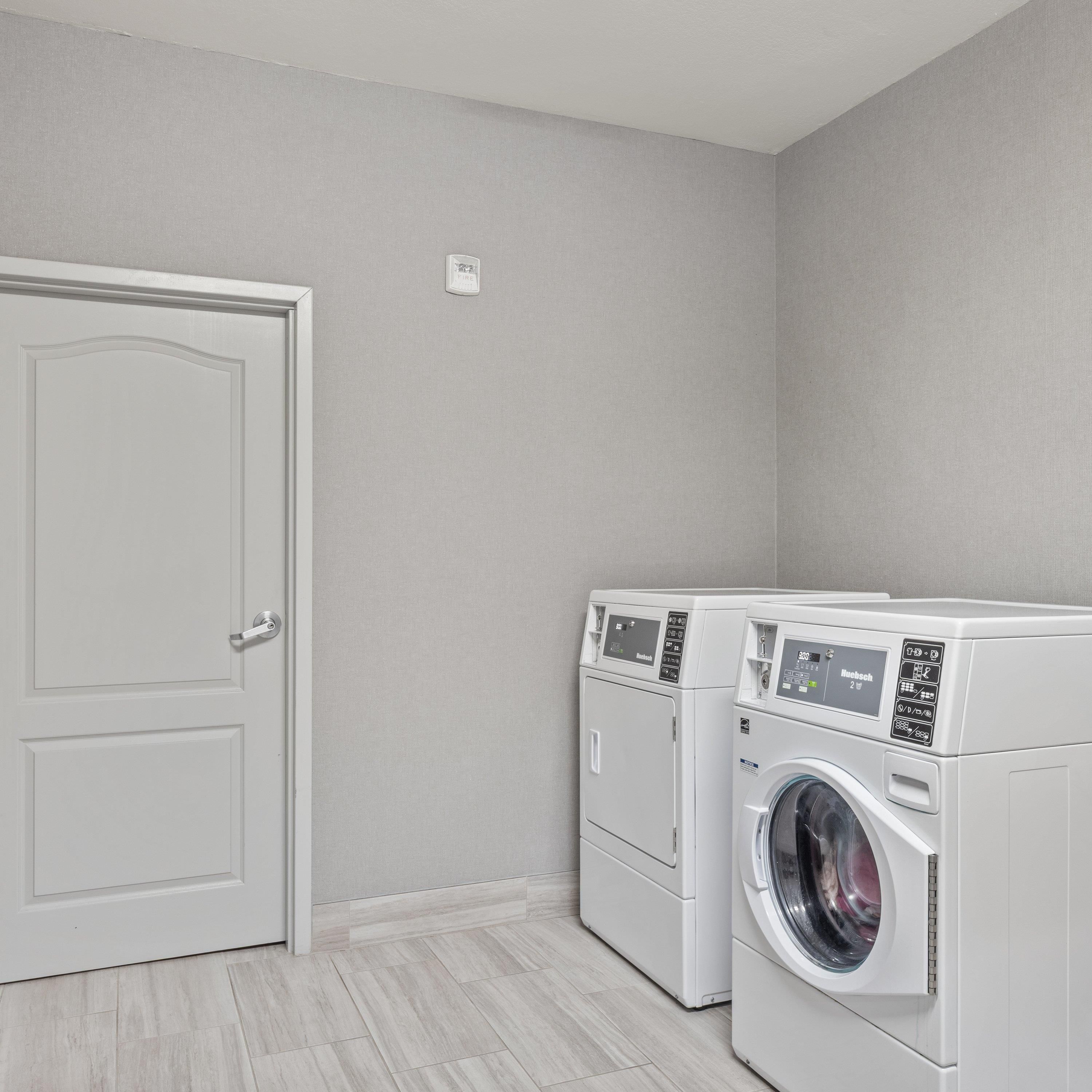 A laundry room with two front-loading washing machines, a door, and a light switch on the wall.
