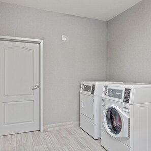 A laundry room with two front-loading washing machines, a door, and a light switch on the wall. - Hampton Inn & Suites Denison (Denison)