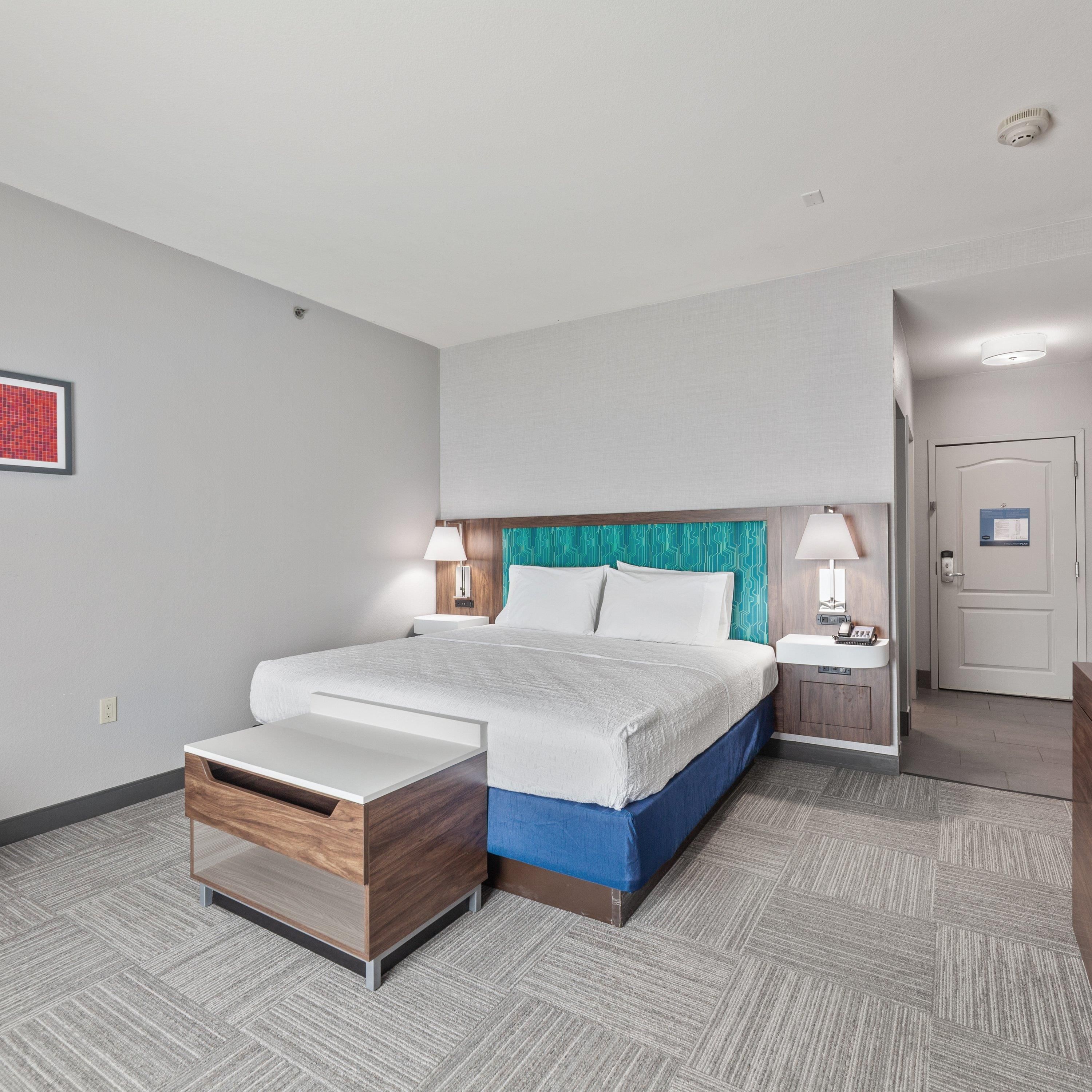 A hotel room with a bed, bedside tables, a desk, and a door.