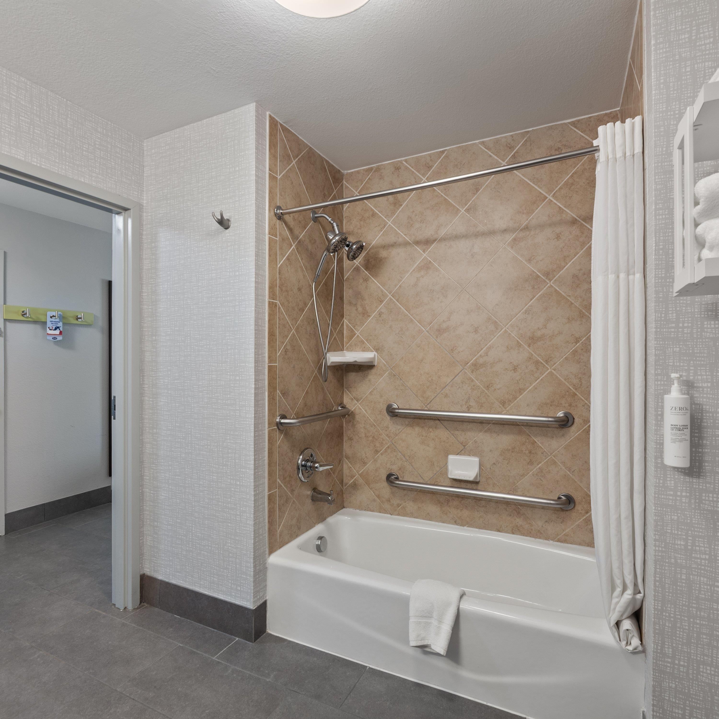 A modern bathroom with a walk-in shower, grab bars, a bathtub, and a toilet.