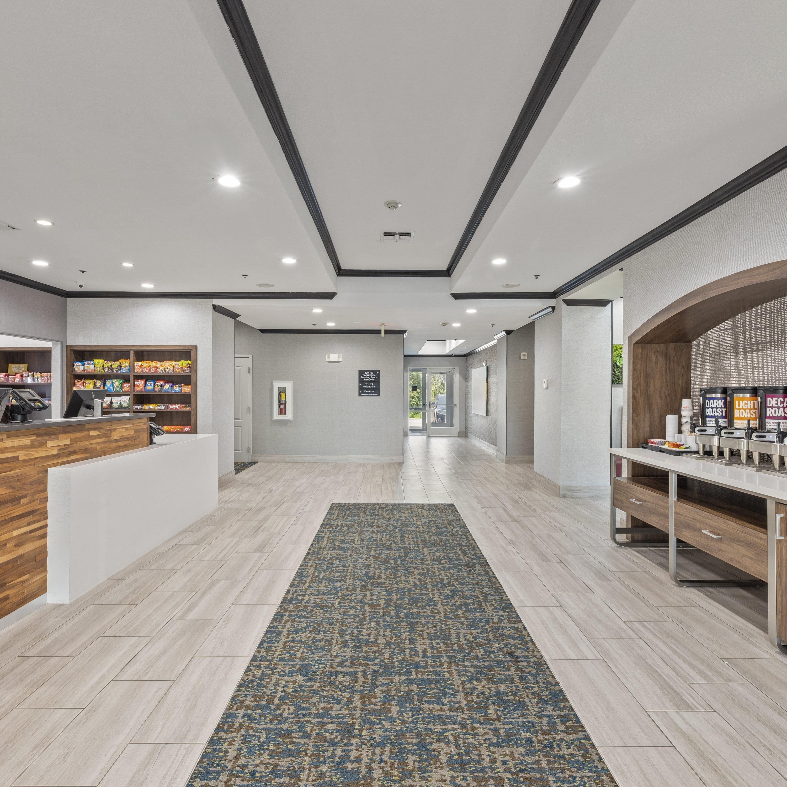 A hotel lobby with a reception desk, a coffee station, and a view of the outdoor area.