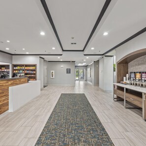 Un vestíbulo de hotel con mostrador de recepción, estación de café y vistas al área exterior.
