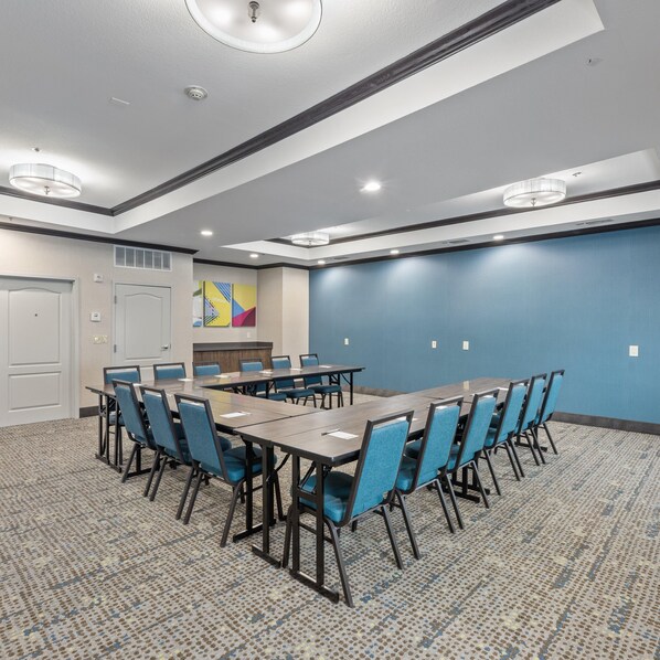 Un salón de conferencias con una larga mesa, sillas azules y piso alfombrado.