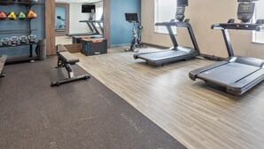Un gimnasio con cintas de correr, una banca de pesas, pesas de mancuerna y pelotas de ejercicio.