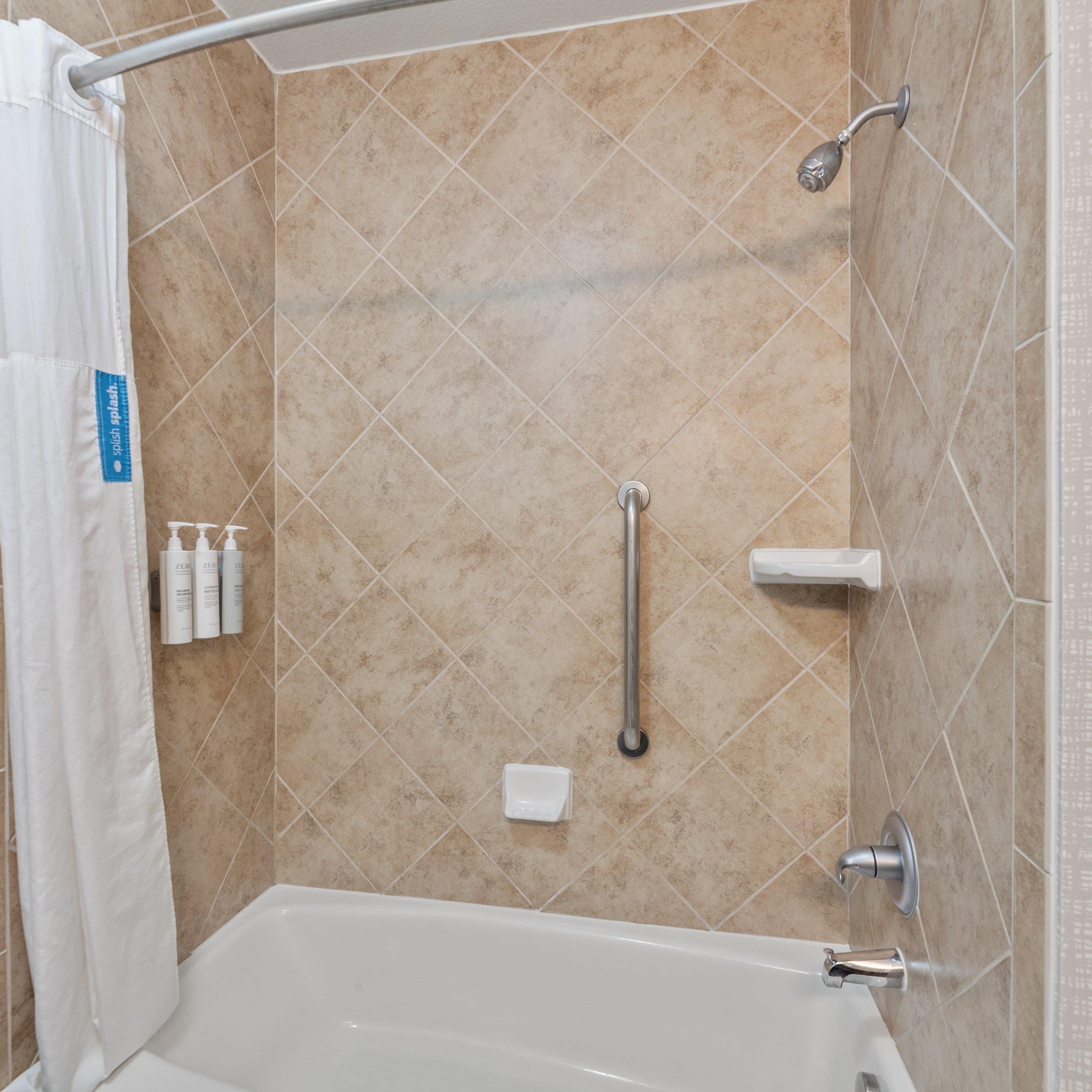 A bathroom with a bathtub, a shower, and a handrail.