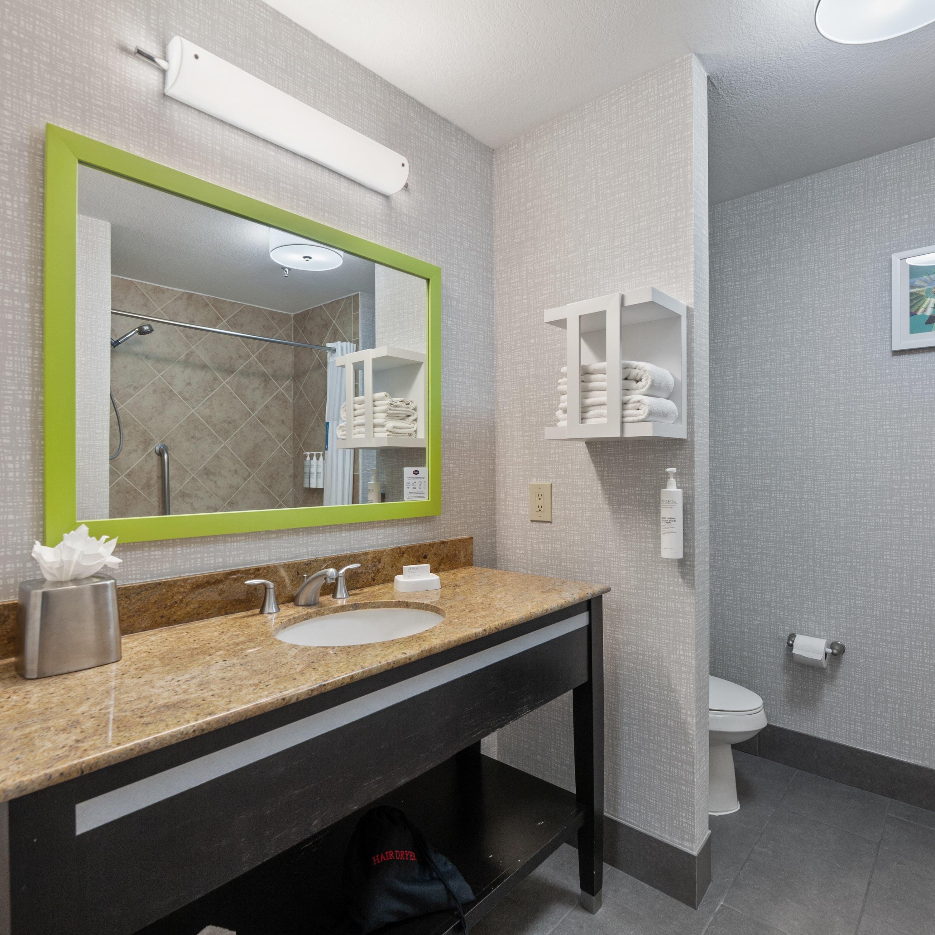 A bathroom with a granite countertop, a sink, a mirror with a green frame, a towel rack, and a toilet.