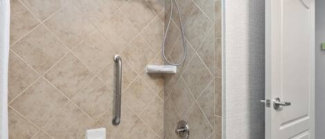 A modern bathroom with a bathtub, shower, and handrails.