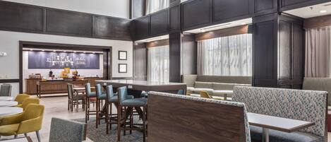 Een moderne hotelentree met een centraal gelegen bar, zithoekjes en grote ramen.