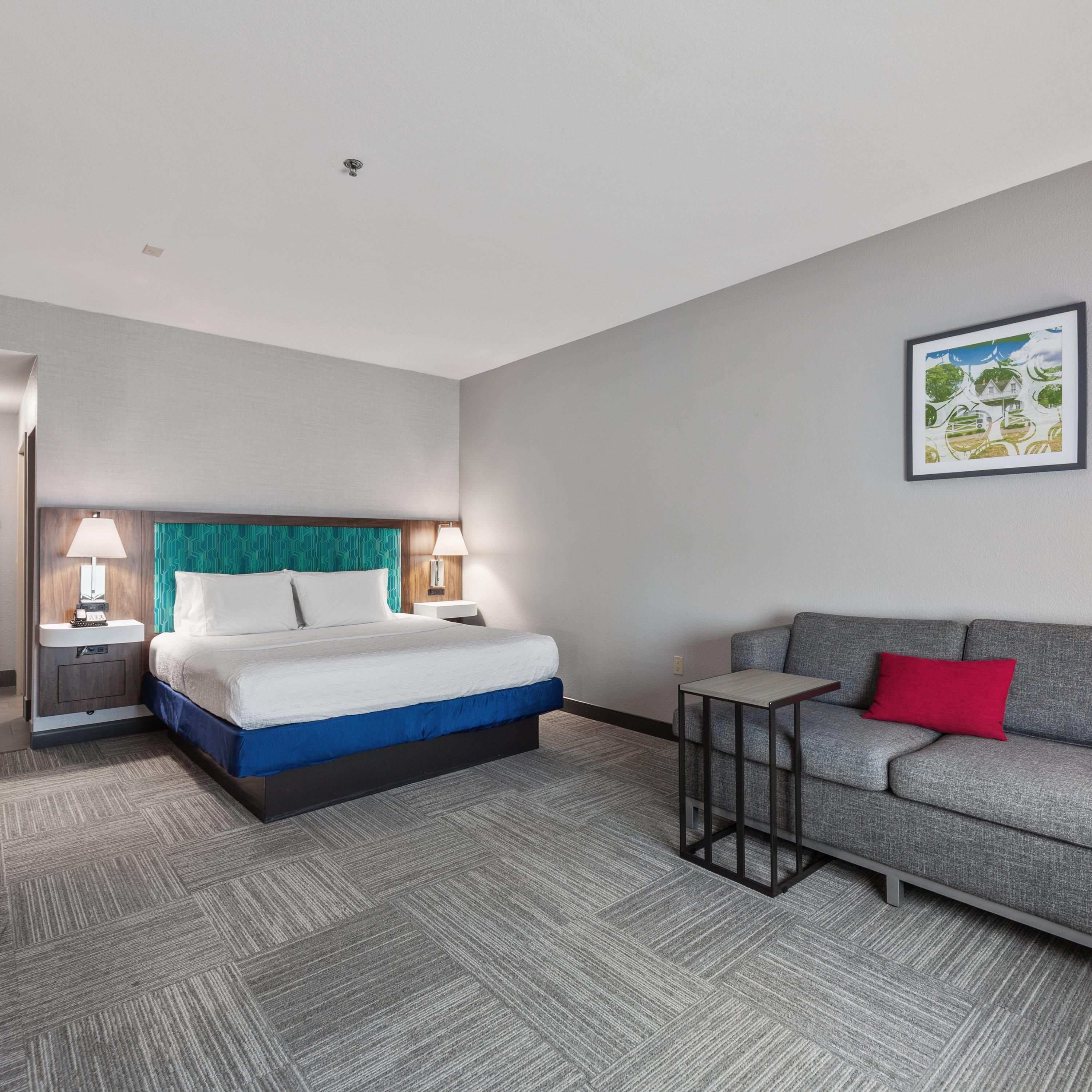 Una habitación de hotel con una cama, un sofá, una mesita y un cuadro en la pared.
