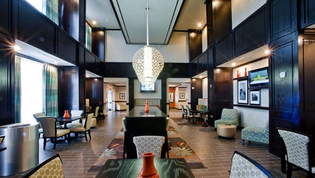 A spacious lobby with a high ceiling, a central chandelier, and a variety of seating arrangements including a long table and multiple chairs. - Hampton Inn & Suites Denison (Denison)