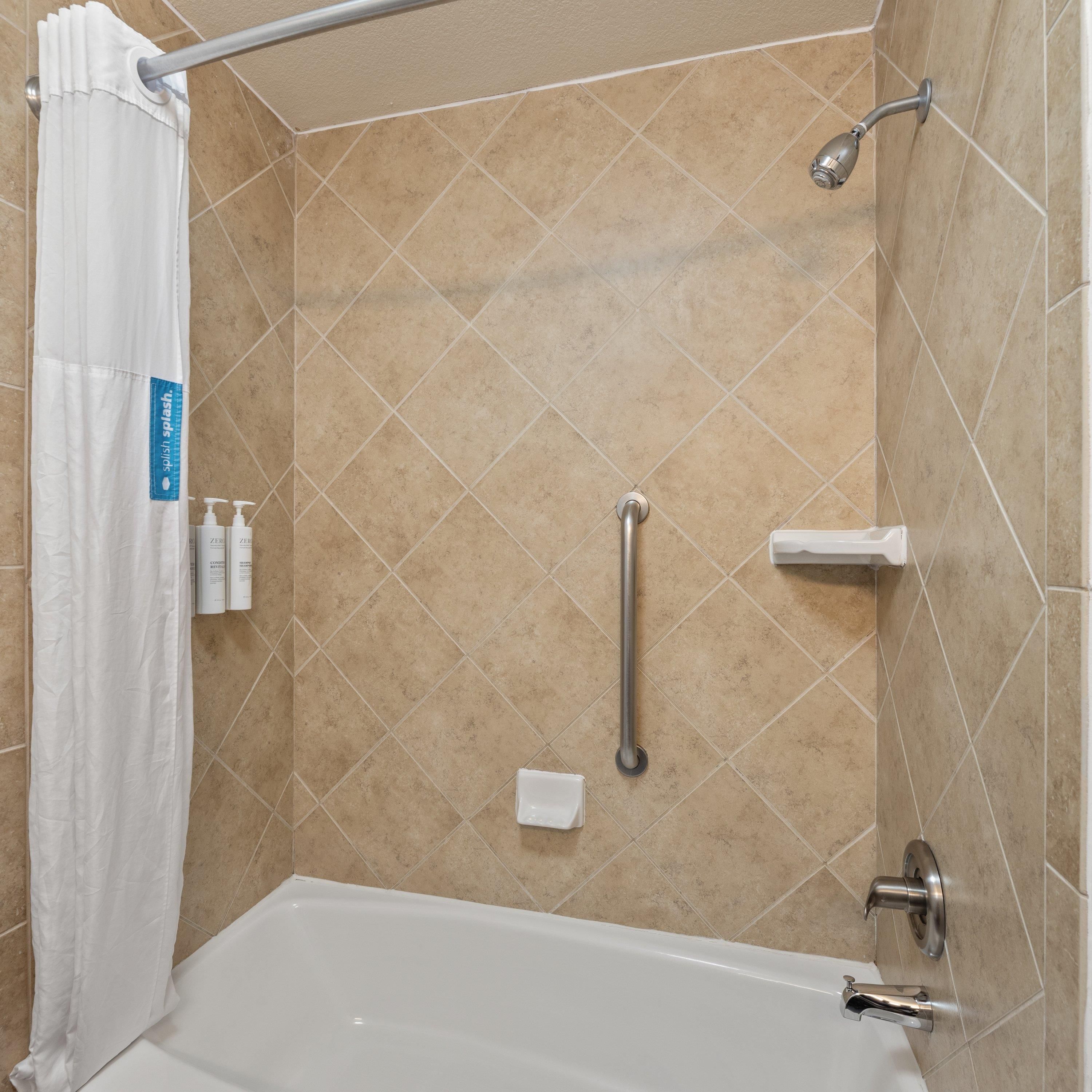 A bathroom with a bathtub, a shower, and a handrail.