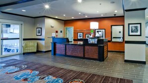 A hotel reception area with a reception desk, a chair, a framed welcome sign, and a wall-mounted lamp. - Hampton Inn & Suites Denison (Denison)