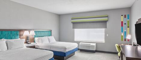 Quarto de hotel com duas camas, uma escrivaninha, uma cadeira, televisão e janela com persianas.