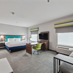 Una habitación de hotel con cama, escritorio, silla, televisión y aire acondicionado.