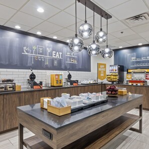 A breakfast area with a long counter, various food items, and a chalkboard with food-related drawings. - Hampton Inn & Suites Denison (Denison)