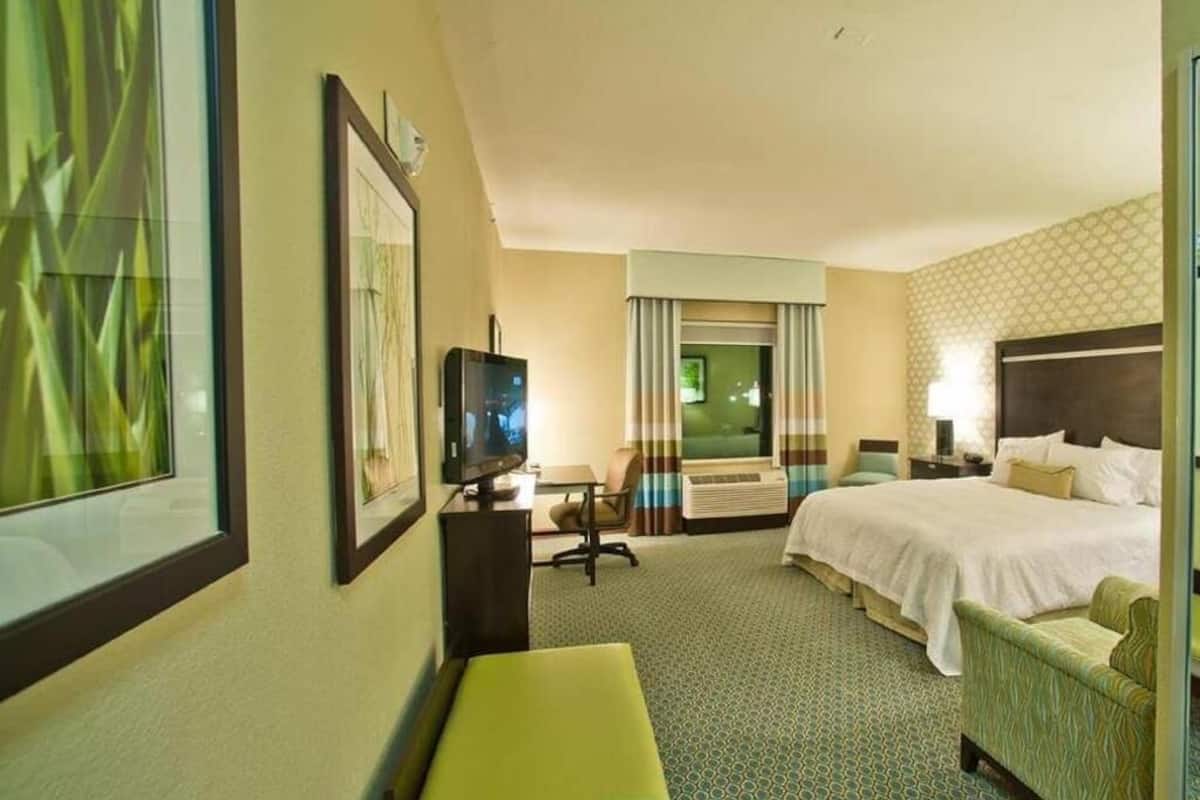 Una habitación de hotel con cama, escritorio con televisor, silla y ventana con cortinas.