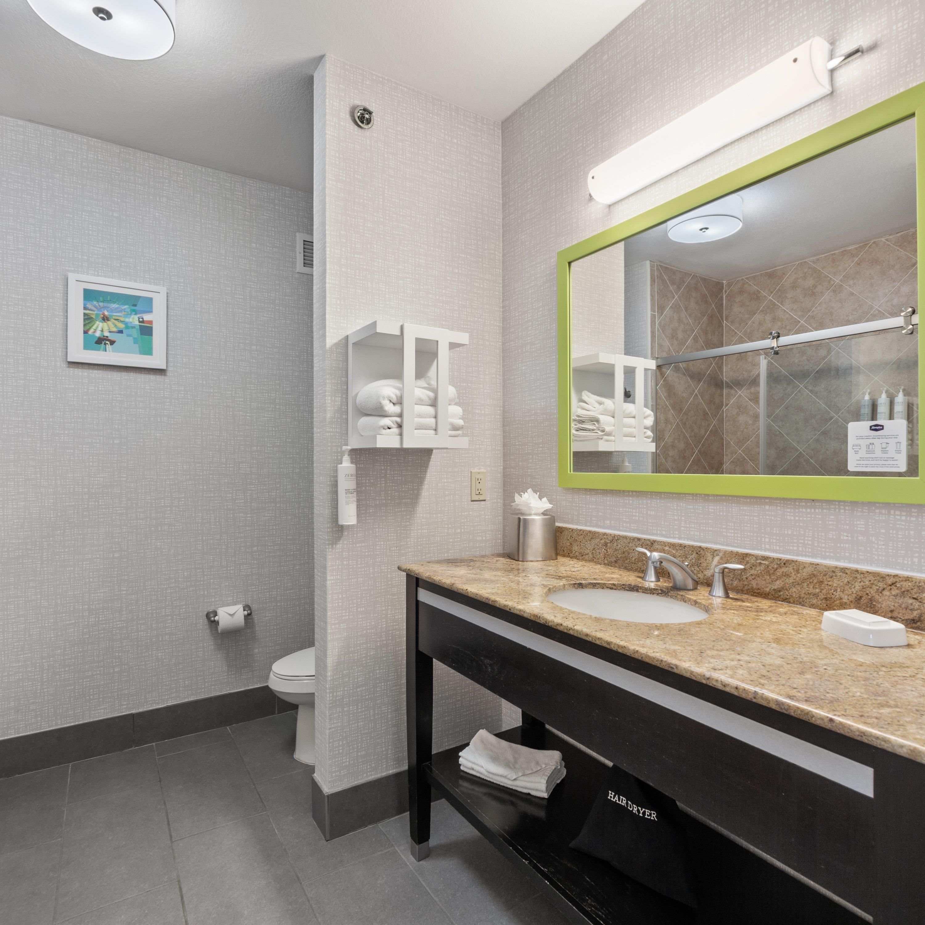 Un baño moderno con encimera de granito, un espejo grande y un secador de pelo.