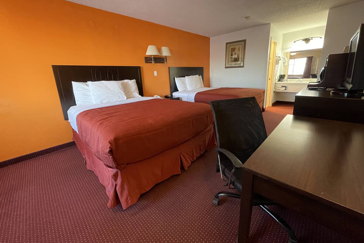 A hotel room with two beds, a desk, a chair, and a television.