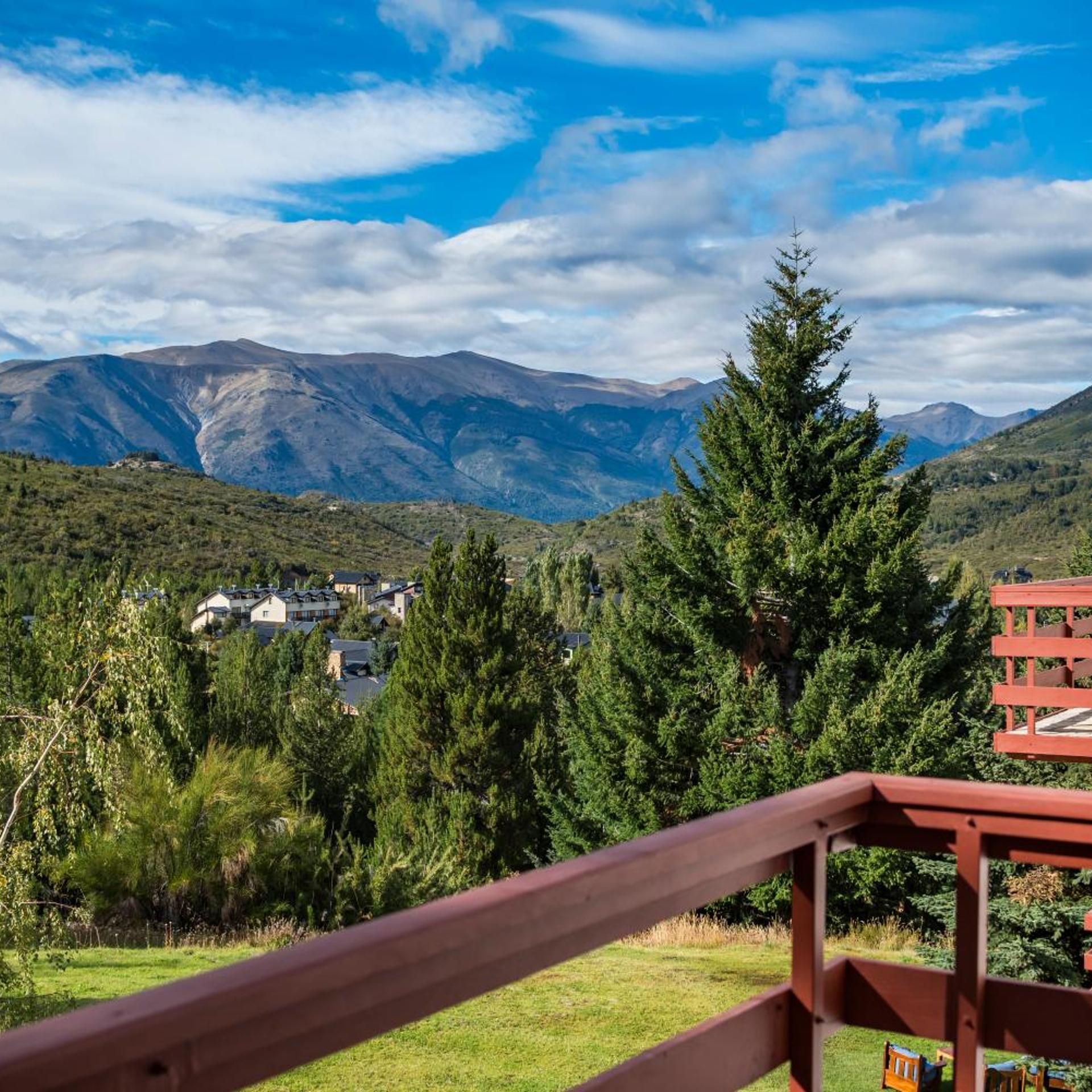 Un paisaje montañoso con cielo despejado, una terraza de madera y vistas a casas en el valle.