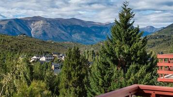 Un paisaje montañoso con cielo despejado, una terraza de madera y vistas a casas en el valle.