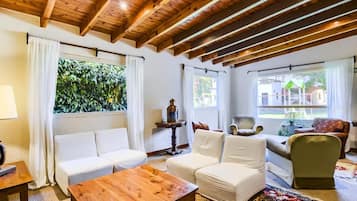 A cozy living room with a wooden ceiling, white sofas, a wooden coffee table, and a patterned rug.
