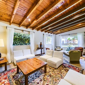 Un salon chaleureux avec un plafond en bois, des canapés blancs, une table basse en bois et un tapis à motifs.