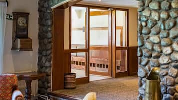 A room with a stone wall, a wooden door leading to an outdoor area, a vintage clock, and a rustic chair.
