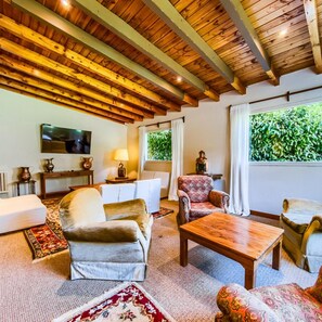 Een gezellige woonkamer met een houten plafond, een televisie, een bank, een gestreept fauteuil en een salontafel.