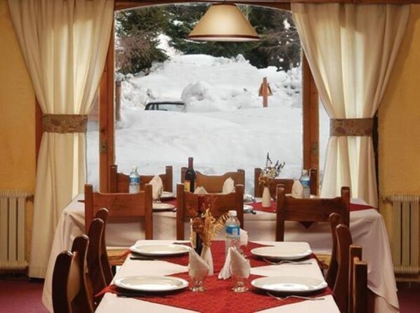 Une table à manger dressée pour quatre personnes, avec vue sur un paysage enneigé par la fenêtre.