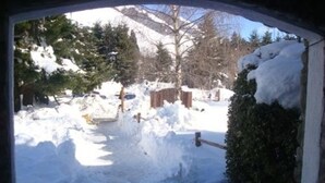 Escena nevada al aire libre con una valla de madera, un sendero cubierto de nieve y una montaña al fondo.