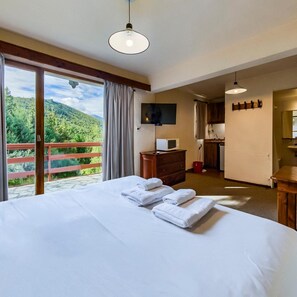 Een hotelkamer met een bed, een televisie, een houten dressoir, een balkon met uitzicht op groen, en een kitchenette.