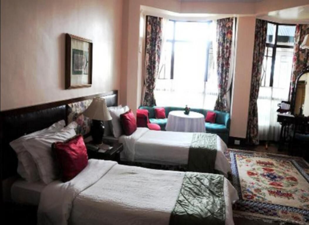 A hotel room with two beds, a sofa, a small round table, and a large window with curtains.