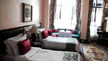 A hotel room with two beds, a sofa, a small round table, and a large window with curtains.