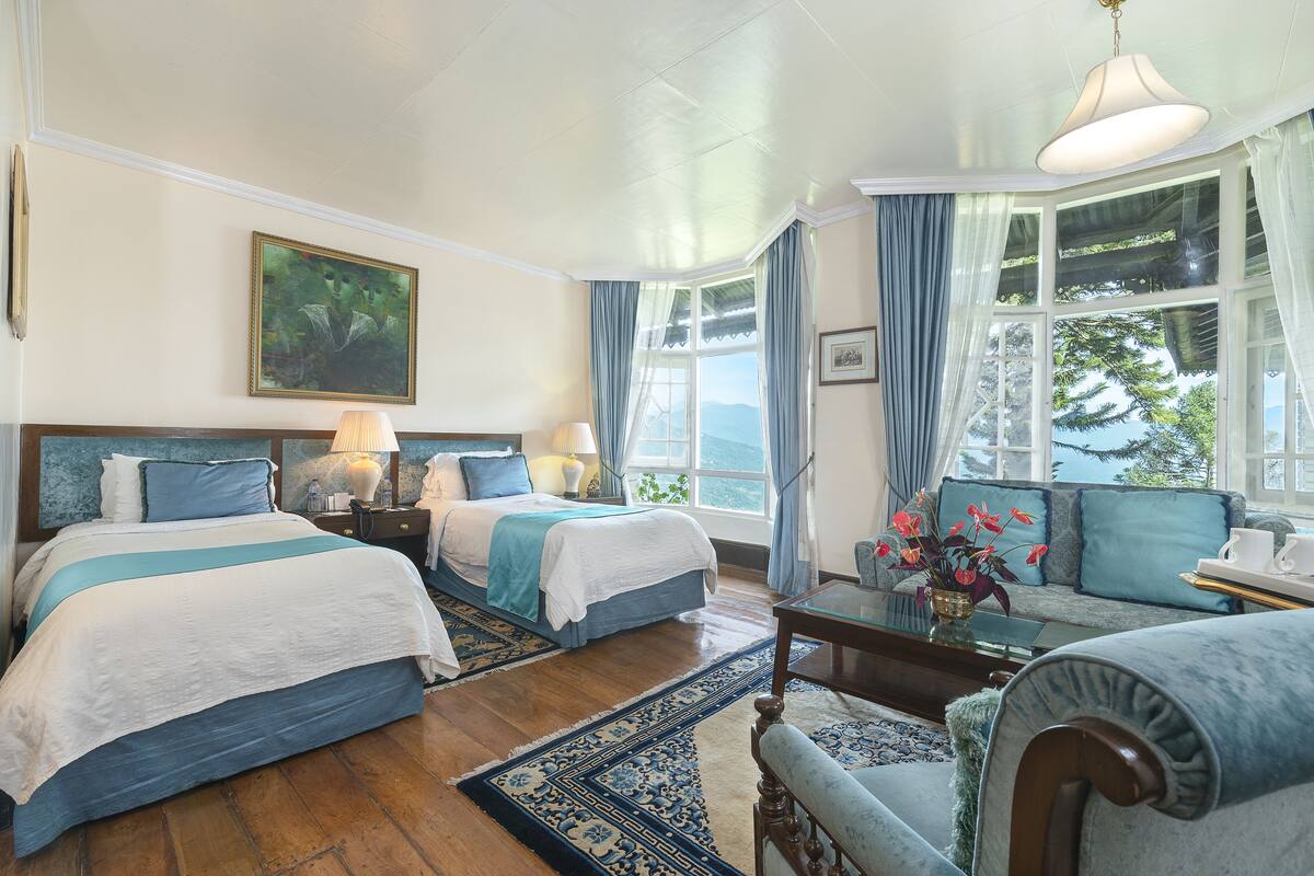 A hotel room with two beds, a sofa, a coffee table, and a large window with a view.