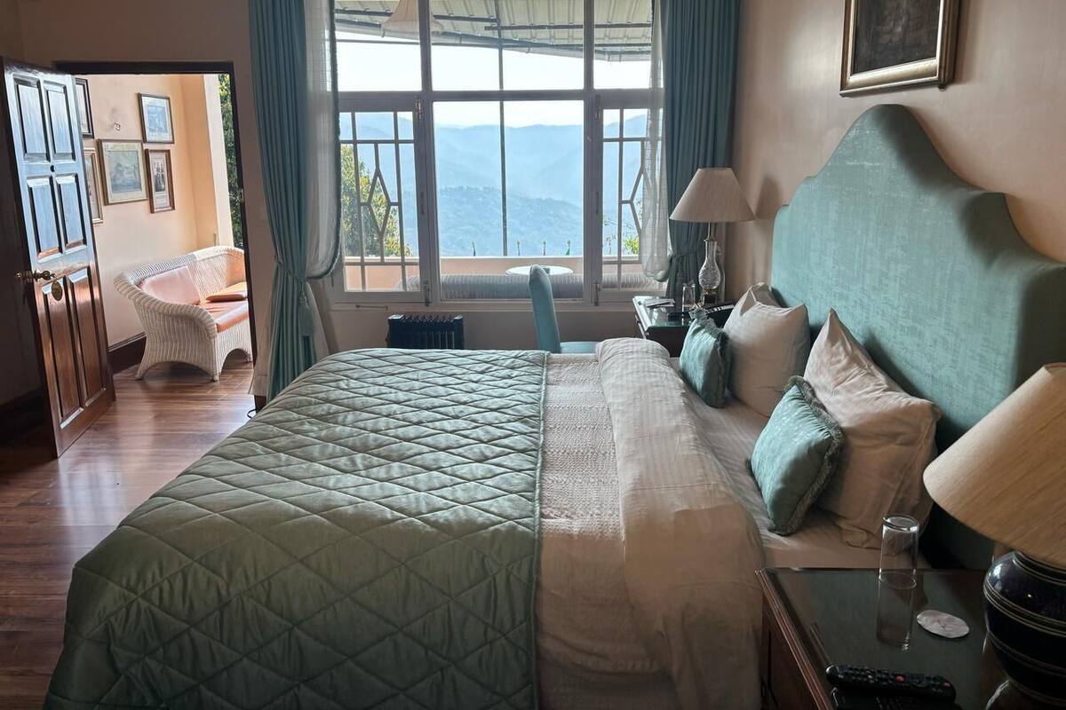 A hotel room with a large bed, a view of the mountains, a chair, and a table with a lamp.