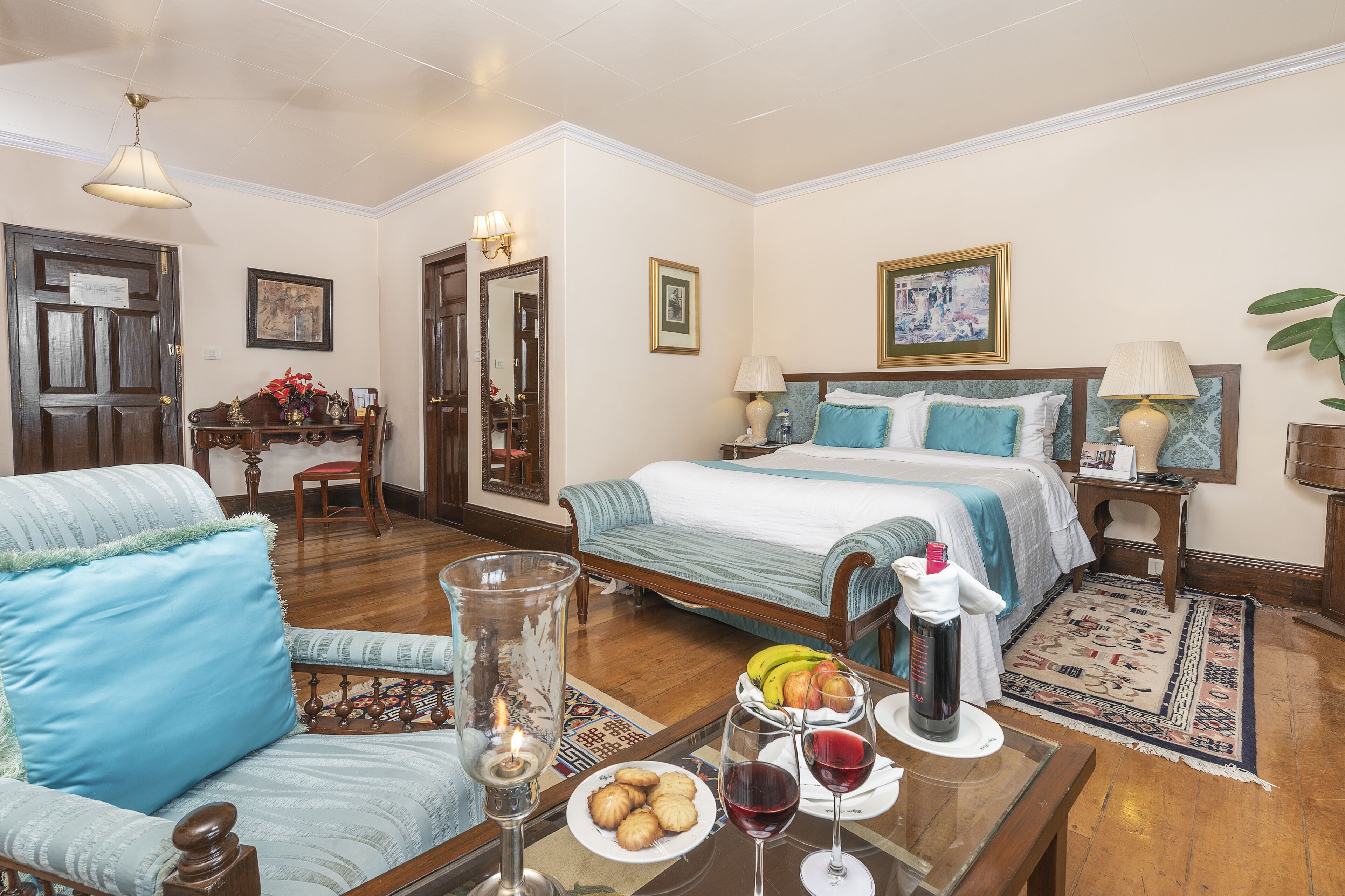 Habitación de hotel con cama, una silla, una mesa con fruta y vino, y una lámpara.