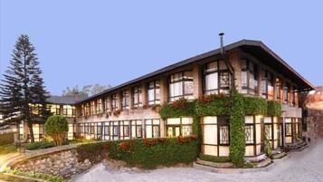 A multi-story building with a stone facade, large windows, and a landscaped garden with red flowers.