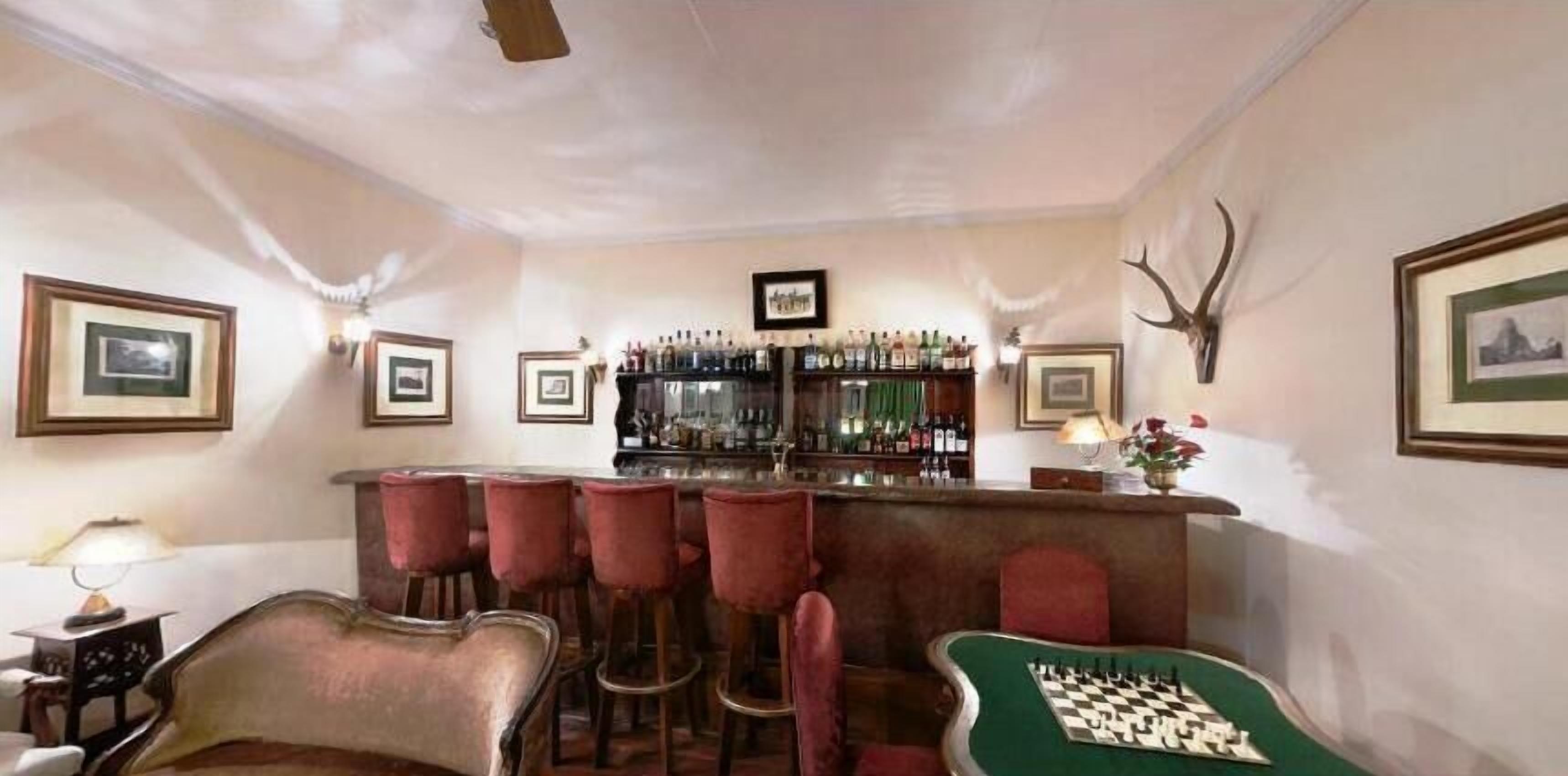 A bar area with a chess table, red bar stools, framed pictures, and a liquor display.
